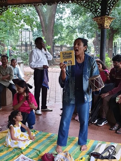 An expressive moment of storytelling, holding up the book 'Kahaani Puraani'. My goal is to bring the characters and emotions of the story to life for the audience.