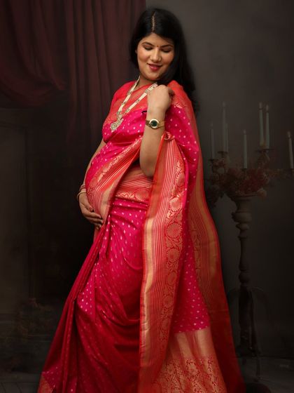 A solo portrait of a mom-to-be glowing in a bright pink saree. The simple, dark background makes the vibrant color and her joyful expression the focus of the image.