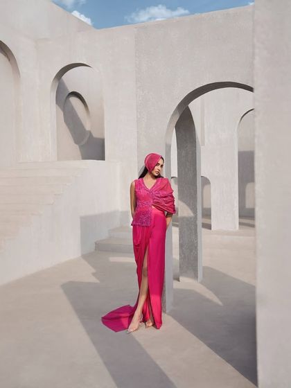 A burst of hot pink, sheer mesh, and movement. This look flows like color through a prism, with a draped sleeve and sculpted skirt that shape the body with effortless drama.