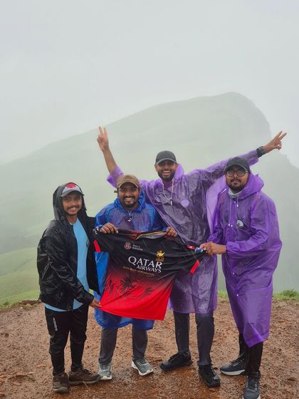 A group of friends and RCB fans celebrating with a team jersey at the top of Netravathi peak.