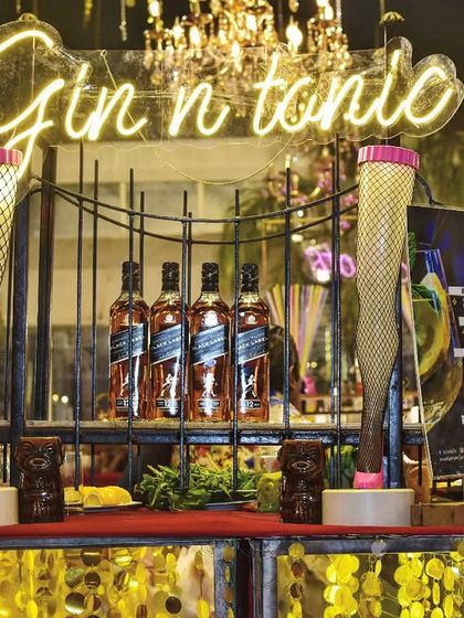 A stylish display of Johnnie Walker Black Label under a 'Gin n tonic' neon sign. I create visually appealing liquor displays that highlight the premium brands available at your event.