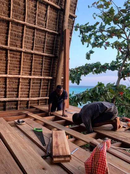 Local craftsmen at work on the wooden floor of the Kizikula spa. The entire structure is handmade using local materials and techniques, providing a stunning view of the ocean through the thatched roof structure.