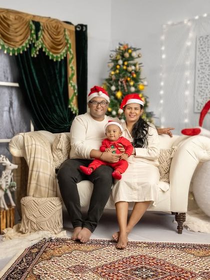 A classic family portrait with everyone seated comfortably on the couch. The baby's bright red outfit adds a perfect pop of festive color.