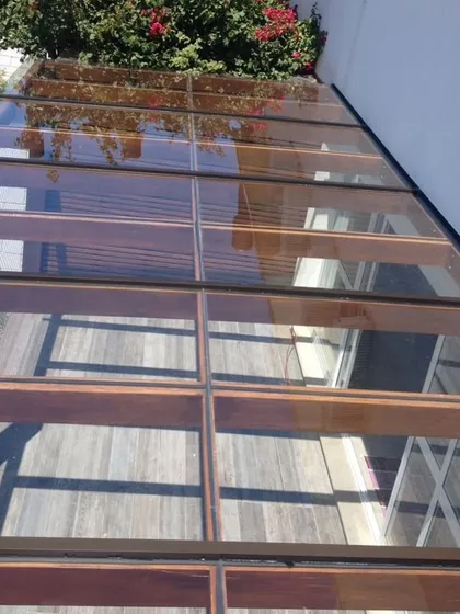 A top-down view of a glass pergola with wooden rafters. This hybrid design combines the transparency of glass for rain protection with the warmth of wood for a natural, shaded effect.