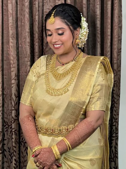 Bride Namita looks absolutely radiant in her golden silk saree. Her look is a perfect example of classic Kerala bridal styling, with layers of gold necklaces and a happy, confident smile.