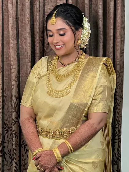 Bride Namita in a beautiful golden tissue silk saree. The soft glow of the saree is complemented by her traditional gold jewellery and jasmine flowers in her hair.