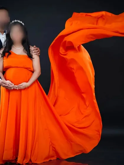 This vibrant orange one-shoulder gown with a long, flowing tail makes a bold and beautiful statement for a studio maternity photoshoot.