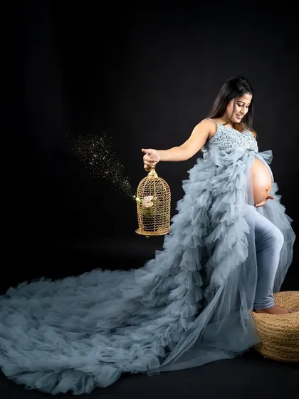 A whimsical and creative portrait. The mom-to-be holds a golden birdcage as sparkles emerge, all while wearing a stunning blue ruffled gown with an open front.