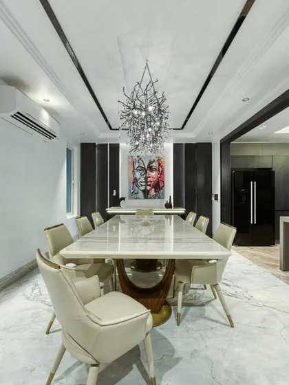 The dining area of the Gallery House, with a long marble table and elegant upholstered chairs. A branch-like chandelier with crystal droplets adds a touch of organic glamour.