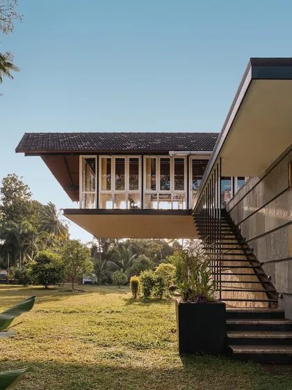 A dramatic cantilevered volume with extensive glazing appears to float above the landscape, showcasing a bold modern intervention in this Kerala home.