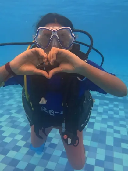 A camper makes a heart shape with her hands underwater, sharing her love for the new skills she's learning in our scuba program.