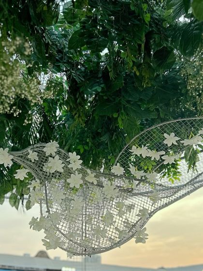 A close-up of a wire mesh bird sculpture adorned with delicate white flowers, hanging amidst lush greenery. This detail highlights the artistic and nature-inspired elements of the decor.