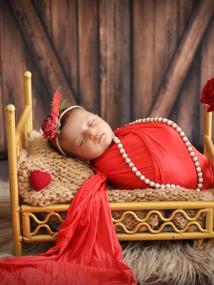 A dramatic and romantic setup in red. The baby sleeps on a tiny bed, adorned with pearls, creating a portrait that is both bold and beautiful.
