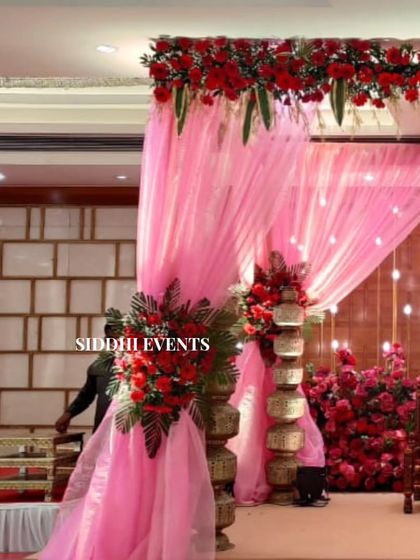 A side view of the red and pink mandap, showing the traditional tiered 'matkas' and the warm glow of the lights behind the seating area.