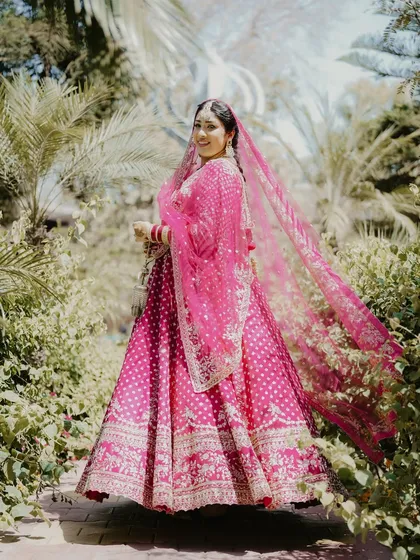 A stunning full-length portrait of the bride in her bright pink Anand Karaj lehenga. The flowing dupatta and the lush green background make for a vibrant and beautiful shot.