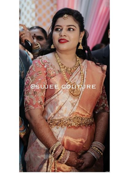 A candid moment capturing the beauty of this bride. Her custom peach-colored blouse features delicate floral embroidery on sheer sleeves, adding a soft and romantic touch to her wedding saree.