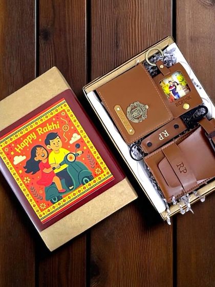This Rakhi gift set features a collection of personalized vegan leather items in a classic tan color, including a passport cover, keychain, and wallet, presented in a box with a festive "Happy Rakhi" sleeve.