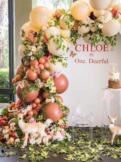 A "deer-ful" first birthday celebration set in an enchanted forest. This lush design combines a beautiful balloon and floral arch with sweet deer figures and scattered leaves on the floor for a truly immersive woodland experience.
