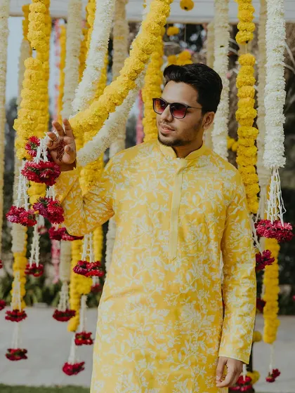 A portrait of the groom looking dapper in his yellow printed kurta, standing against a backdrop of marigold garlands.