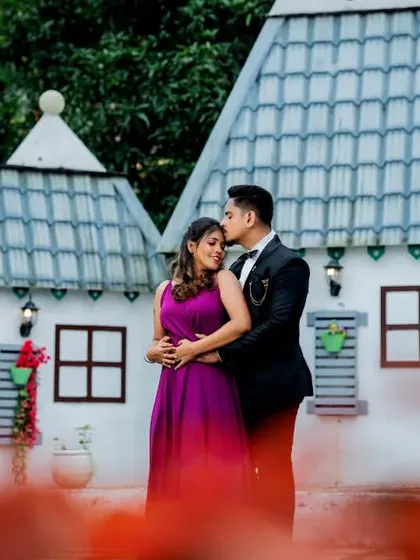 A tender forehead kiss framed by colorful flowers at a pre-wedding set. This shot uses foreground elements to create depth and focus on the couple's intimate moment.