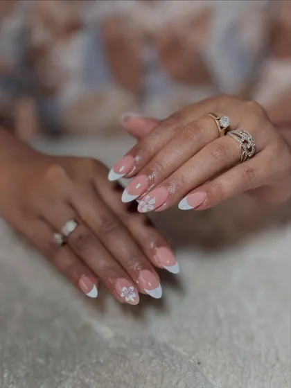 A delicate and pretty design on almond-shaped nails. This is a classic French manicure with subtle, hand-painted white floral art on the ring fingers.