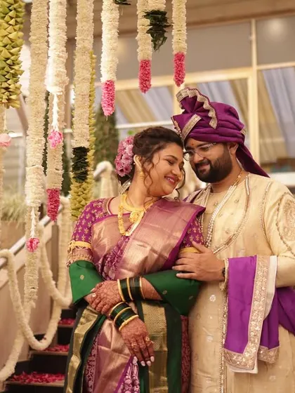 A romantic portrait of the couple amidst the wedding decorations. The bride's classic Maharashtrian look, with a bindi and gold jewelry, is perfectly complemented by the groom's embroidered sherwani and pheta.