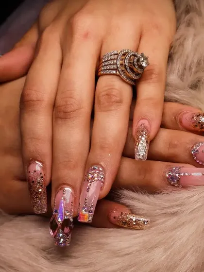 A close-up of a full set of custom jeweled nail extensions. This look combines glitter, iridescent crystals, and a flawless shape to create a truly luxurious and eye-catching manicure perfect for weddings or celebrations.