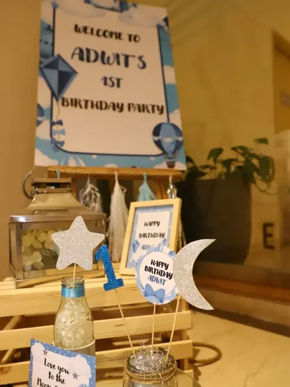 The welcome table for Adwit's first birthday. It features a personalized sign, themed toppers like stars and a moon, and other small decorative elements on rustic wooden crates.