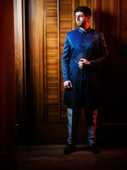 A full-length portrait of the groom, showcasing his unique blue and black reception outfit.
