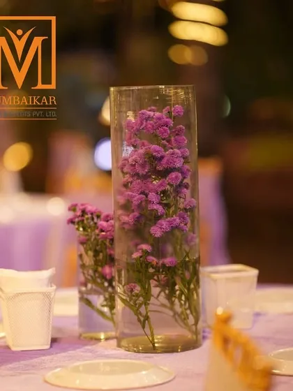 A simple yet elegant centerpiece for a reception table. A tall glass vase filled with purple flowers adds a touch of color and sophistication to the guest dining experience.