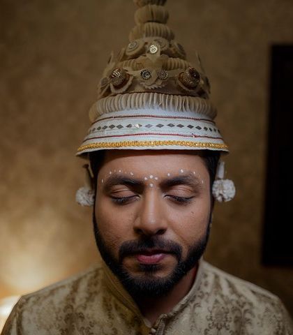 A close-up portrait of the groom with his eyes closed, wearing the traditional Bengali 'topor'. A serene and spiritual moment captured before the wedding.