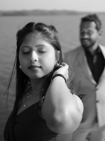 A close-up black and white portrait focusing on the bride-to-be. The soft focus on her partner in the background adds depth and a narrative quality to the image.