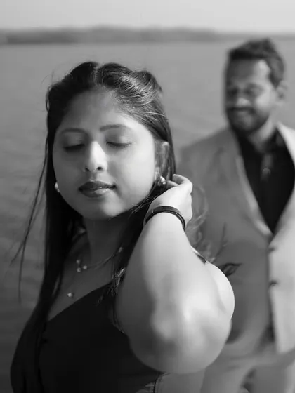 A close-up black and white portrait focusing on the bride-to-be. The soft focus on her partner in the background adds depth and a narrative quality to the image.