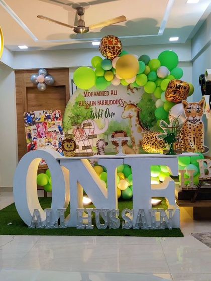 A cozy indoor jungle theme for a first birthday. The setup includes a 'ONE' marquee table, animal cutouts, and a green balloon arch, perfect for a home celebration.