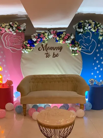 A 'Mommy to be' baby shower stage with a pink and blue theme. The decor includes custom backdrops, floral arrangements, and a light up initial for a personal touch.