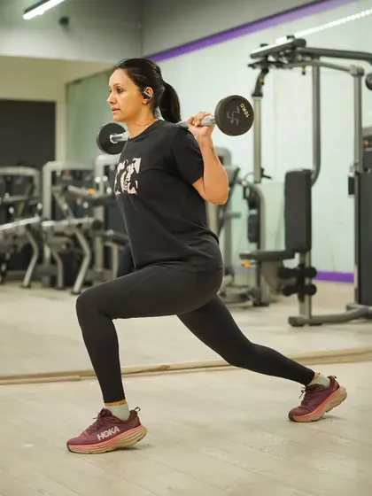 A member performs barbell lunges, a challenging exercise that enhances lower body strength, balance, and coordination.