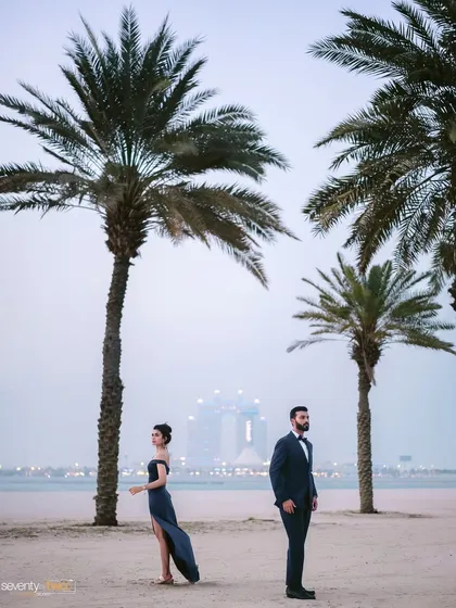 A dramatic portrait on the beach, with the Dubai skyline in the distance. The palm trees frame them perfectly, creating a sense of place and a touch of glamour.
