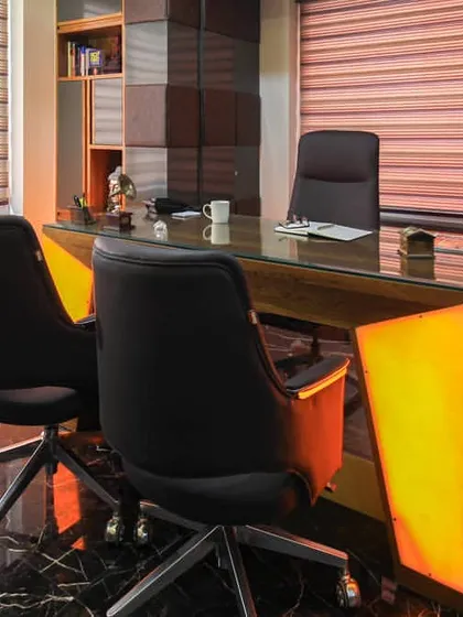 A close look at a finished director's room where we used premium materials to make a statement. The desk features a backlit onyx panel that creates a warm glow, complemented by the dark marble flooring and custom wood veneer shelving.