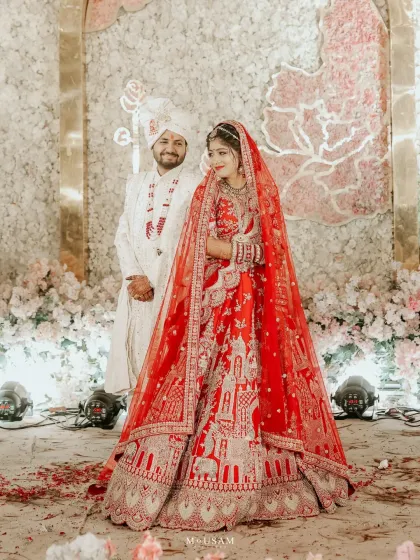 A stunning couple portrait where the bride's vibrant red lehenga complements the groom's classic white sherwani. This showcases how coordinated, not matching, outfits can create a sophisticated and visually striking look.