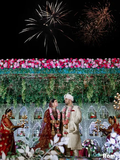 A spectacular shot of the couple at their Varmala ceremony, with fireworks lighting up the night sky behind them. This image captures the grandeur and magic of their wedding celebration.