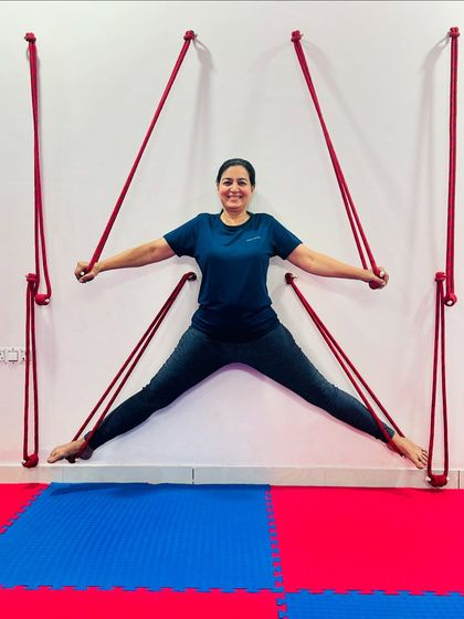 The wall ropes allow for creative and deep stretches. This student smiles as she holds a supported wide-legged stance, feeling the release in her hips and inner thighs.