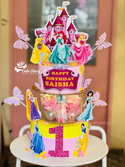 A grand princess-themed rotating cake for a first birthday. This three-tier masterpiece features a castle, multiple princesses, and a light-up rotating center with more surprises inside.