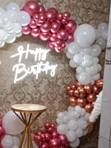 A beautiful balloon ring in metallic pink and white, set up against a wallpapered wall in what appears to be a restaurant or banquet hall space.