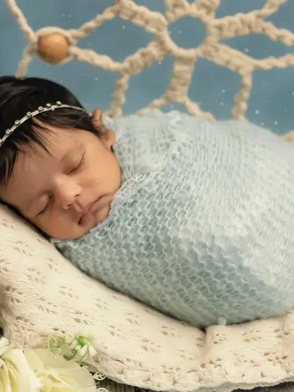A close-up portrait focusing on the baby's peaceful face, swaddled snugly in a soft blue wrap.