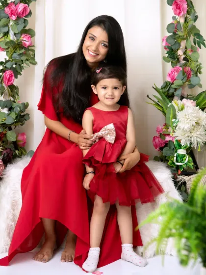 A classic mother-daughter portrait in matching red outfits, both looking at the camera with bright, happy smiles.