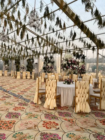 A daytime shot of a beautiful transparent marquee setup, with elegantly woven chair covers and hanging greenery, ready for an evening event.