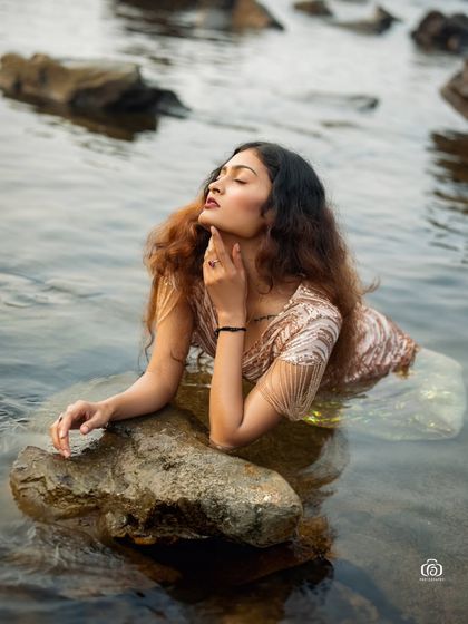 A serene and beautiful portrait of a model in a glamorous gown, sitting in the calm water. The reflection and the soft light create a peaceful and dreamlike image.