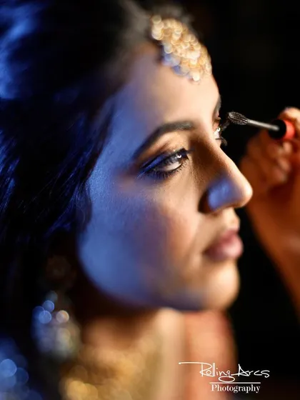 A close-up shot of the bride having her mascara applied. The dramatic blue lighting and focused angle create a cinematic and artistic getting-ready photograph.