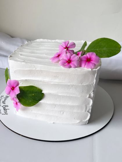 Simple yet elegant. This square cake has a textured white buttercream finish and is decorated with just a few fresh pink flowers and leaves for a minimalist look.