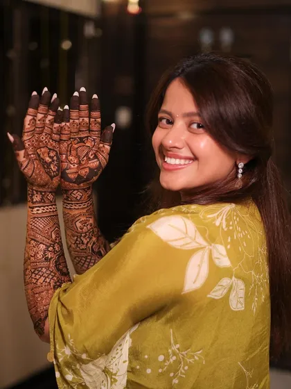 A joyful bride showing both her hands, covered in stunningly detailed mehendi from fingertips to elbow. Her happy smile says it all.